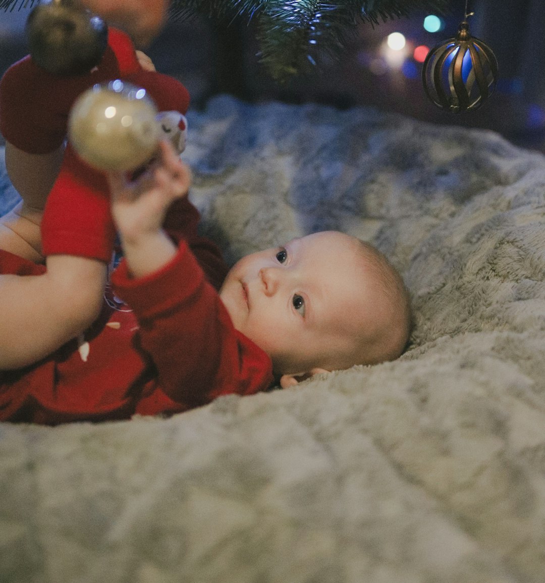 A baby laying on a bed with a christmas tree in the background
